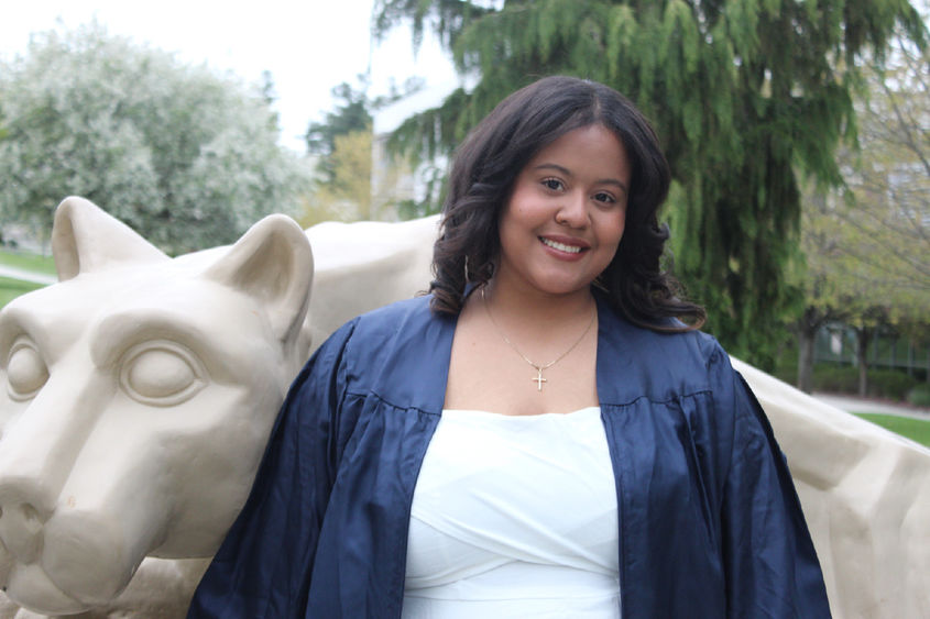 Aidee Santos Acosta poses in front of Nittany Lion Statue in grad gown