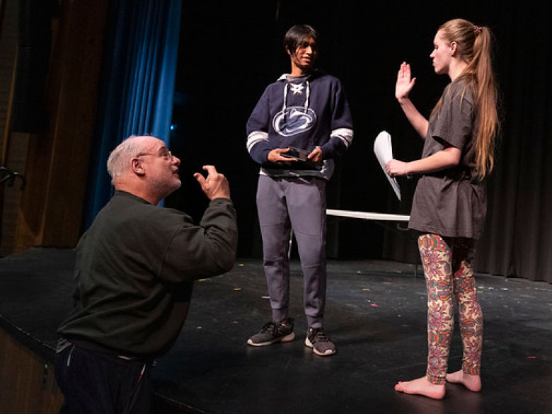 Students run lines on stage with professor in a theatre class
