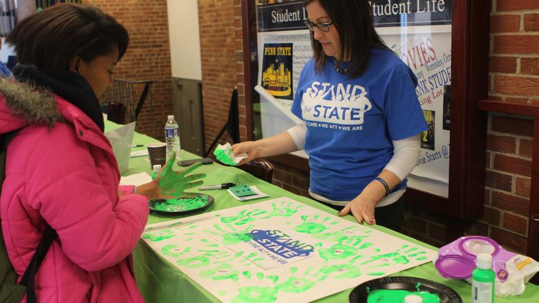 A student prepares to leave a green handprint on a poster