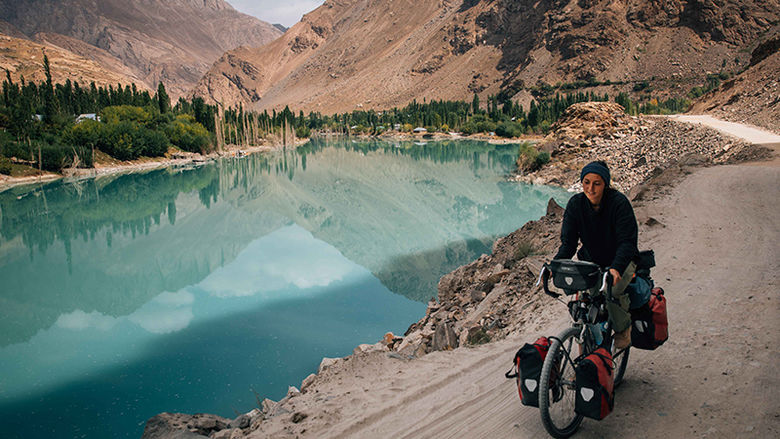 Nicole bikes past a turquoise lake set in a valley between tall rocky mountains