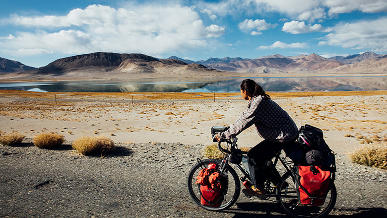 Nicole bikes past a lake on a flat plain, with mountains in the background