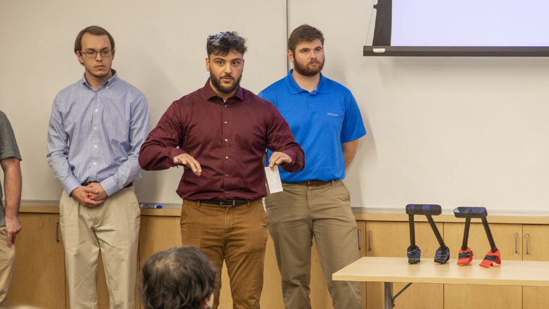 Three male students present portable assistive toilet handles
