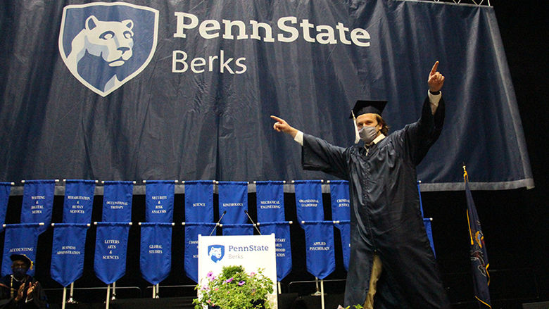 A student crosses the stage, pointing out at the crowd 