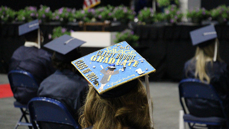 A student wearing a cap decorated to say "I'm a savage, classy, bougie graduate"