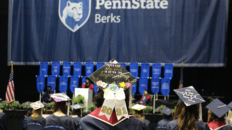 A student faces the stage, wearing a cap decorated to say "What feels like the end is often the beginning."
