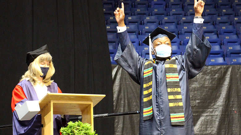 A student crosses the stage in front of Dr. Larson at the podium, arms overhead in victory