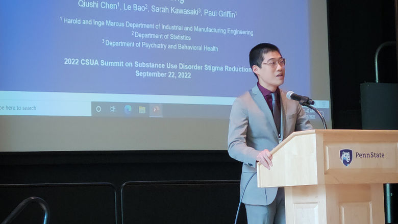 Zixuan Feng, a man in a grey suit, stands at the podium.