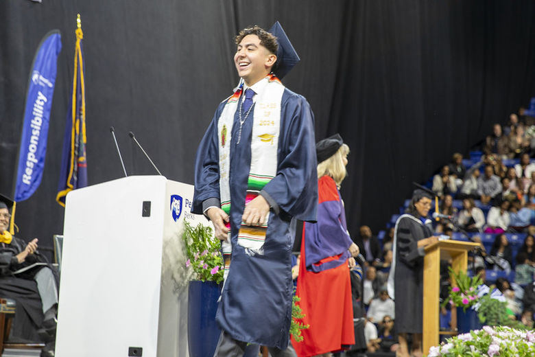 Graduate Rogelio Flores wears cap, gown, and Mexican heritage sash while crossing stage 