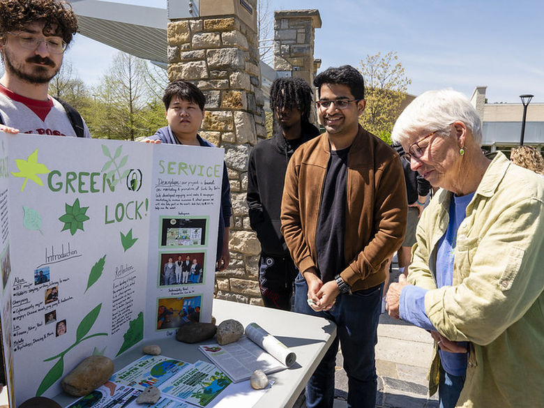 A visitor reviews a sustainability-themed poster project presented by two students.