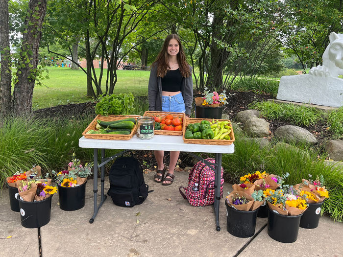 A female student stands behind a table loaded with fresh-cut flowers