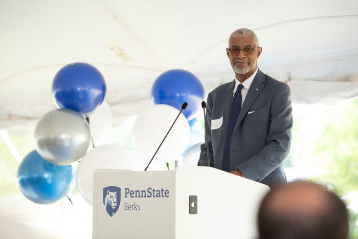 Penn State Berks Chancellor George Grant Jr. standing a podium with the Penn State Berks mark and blue and white balloons in the background.
