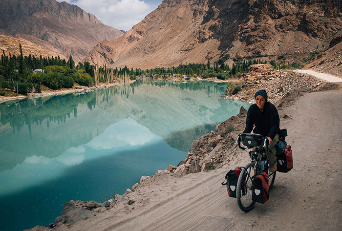 Nicole bikes past a turquoise lake set in a valley between tall rocky mountains