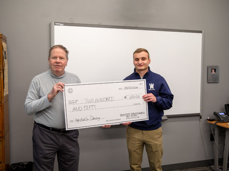 Male student holds check of $250 for photo