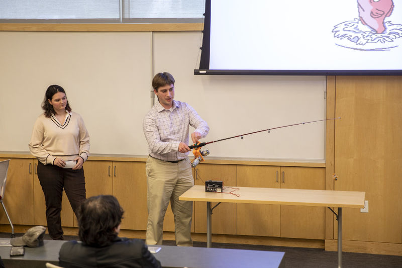 Male student holds adaptive fishing rod to demonstrate to group of attendees