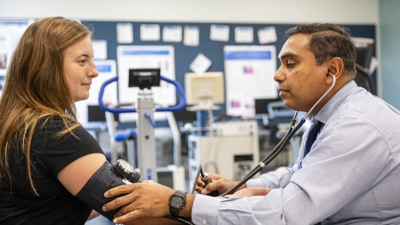 One person wearing a stethoscope takes the blood pressure of another person