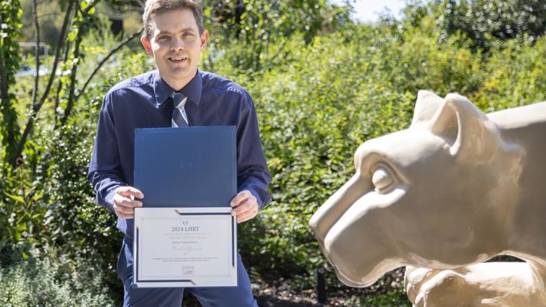 Brett Spencer holding award next to Nittany Lion statue