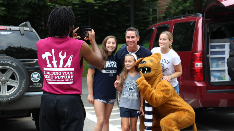 Penn State Berks move-in volunteer taking a photo of an incoming student, her family, and the Nittany Lion.