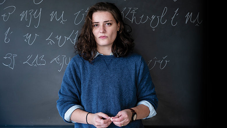 Jannah Martin stands in front of a chalkboard with her constructed language, KFZ, written behind her in chalk.