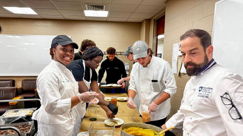 Six students and an instructor wearing chef coats spoon polenta onto plates