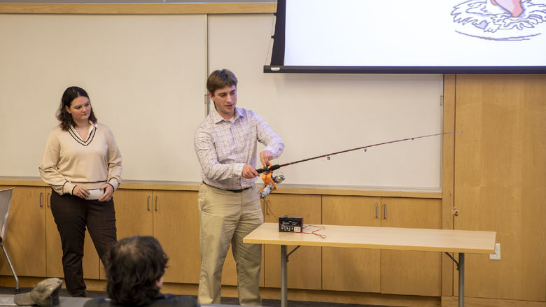 Male student holds adaptive fishing rod to demonstrate to group of attendees