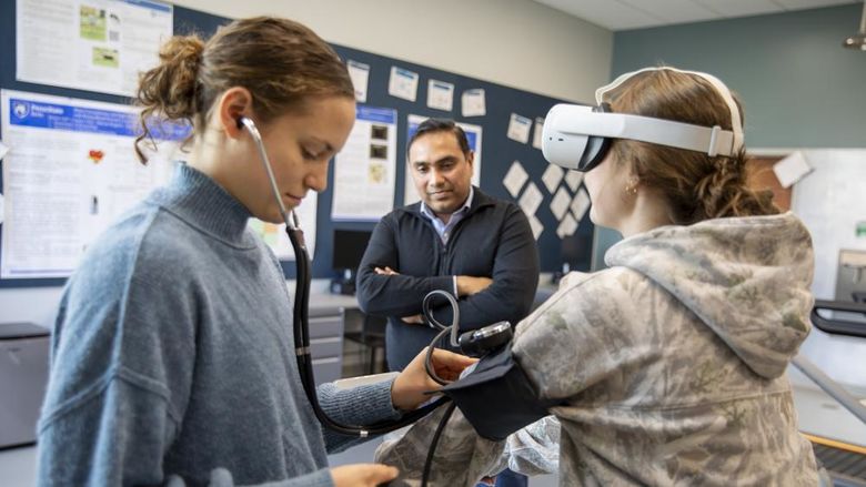 Student takes blood pressure of another student on stationary bike while faculty observes