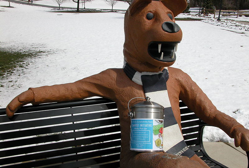 The Nittany Lion statue with a compost container.