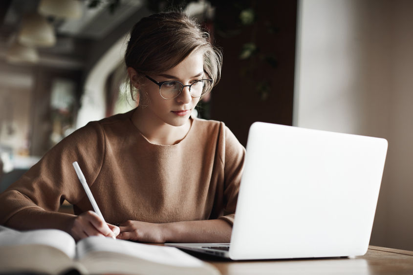 Young woman with sweatshirt and glasses works on her computer