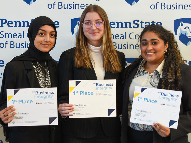 Three female students pose in front of a Penn State Smeal College of Business backdrop holding 1st place certificates