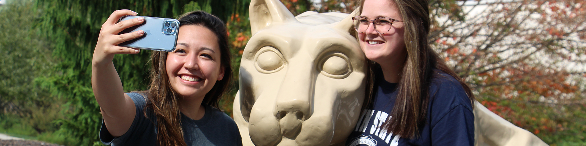 Two female Alumni taking photos with the Nittany Lion Shrine